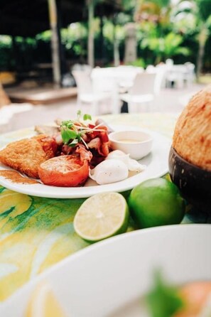 A dining table with a plate of food, including a breaded item, tomato slices, and a small bowl of sauce. - Sands of Rarotonga (Avarua)