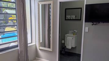 Habitación de hotel con cama, ventana con cortinas, televisor de pantalla plana y baño visible a través de una puerta abierta.
