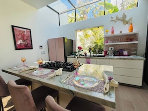 A modern kitchen with a dining area, a gas stove, and a window with a view of greenery. - Pool House 311 by Diana (Jocotepec)