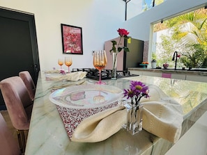 Un comedor con una mesa de vidrio, sillas y un florero con flores.