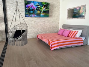 Un dormitorio con una silla colgante, una cama con ropa de cama a rayas y dos obras de arte en la pared.