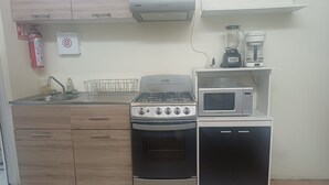 Ett kompakt kök med en gasspis, ugn, mikrovågsugn och en kaffebryggare på en hylla.