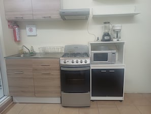 A compact kitchen with a gas stove, oven, microwave, and a coffee maker on a shelf. - Vrbo Property (Toluca de Lerdo)