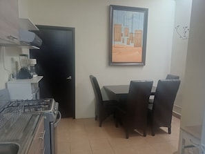 A kitchen with a gas stove, a blender, and a microwave. There is a dining table with four chairs. A door is visible on the left, and a framed picture hangs on the wall above the table. - Vrbo Property (Toluca de Lerdo)