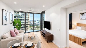 A modern hotel room with a large window, a flat-screen TV, a bed with wooden headboard, and a seating area with a sofa and coffee table. - Queen’s Wharf 1BR + Free Parking | Brisbane CBD (Brisbane)