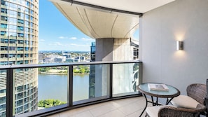 Un balcon doté d’une balustrade en verre, d’une table ronde et d’un fauteuil en osier.