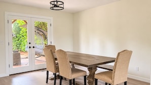 Un comedor con mesa de madera y cuatro sillas, una puerta blanca con paneles de vidrio y una lámpara colgante.