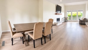Un comedor amplio con una larga mesa de madera y seis sillas tapizadas, un televisor de pantalla plana montado en la pared y vistas al exterior a través de grandes ventanales.