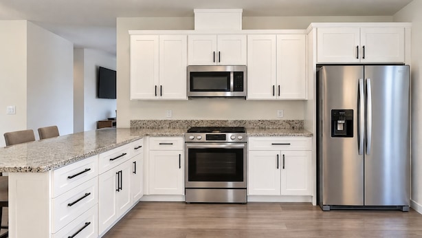 Una cocina moderna con armarios blancos, un refrigerador de acero inoxidable, horno empotrado y microondas.