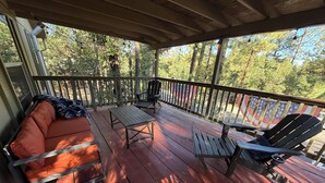 Une véranda abritée avec une table en bois, deux fauteuils Adirondack et un canapé.