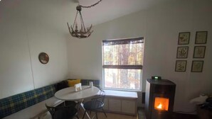 Une pièce chaleureuse avec une table de salle à manger ronde, deux chaises, un banc, une cheminée et une fenêtre avec des stores.
