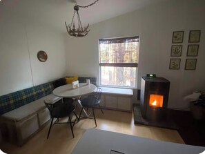 Een gezellige kamer met een ronde eettafel, twee stoelen, een bankje, een open haard en een raam met jaloezieën.