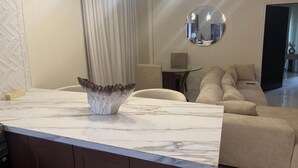 Un soggiorno moderno con un piano di lavoro in marmo, un vaso decorativo, uno specchio rotondo e un divano beige.