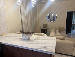 Una sala de estar moderna con encimera de mármol, un jarrón decorativo, un espejo redondo y un sofá color beige.