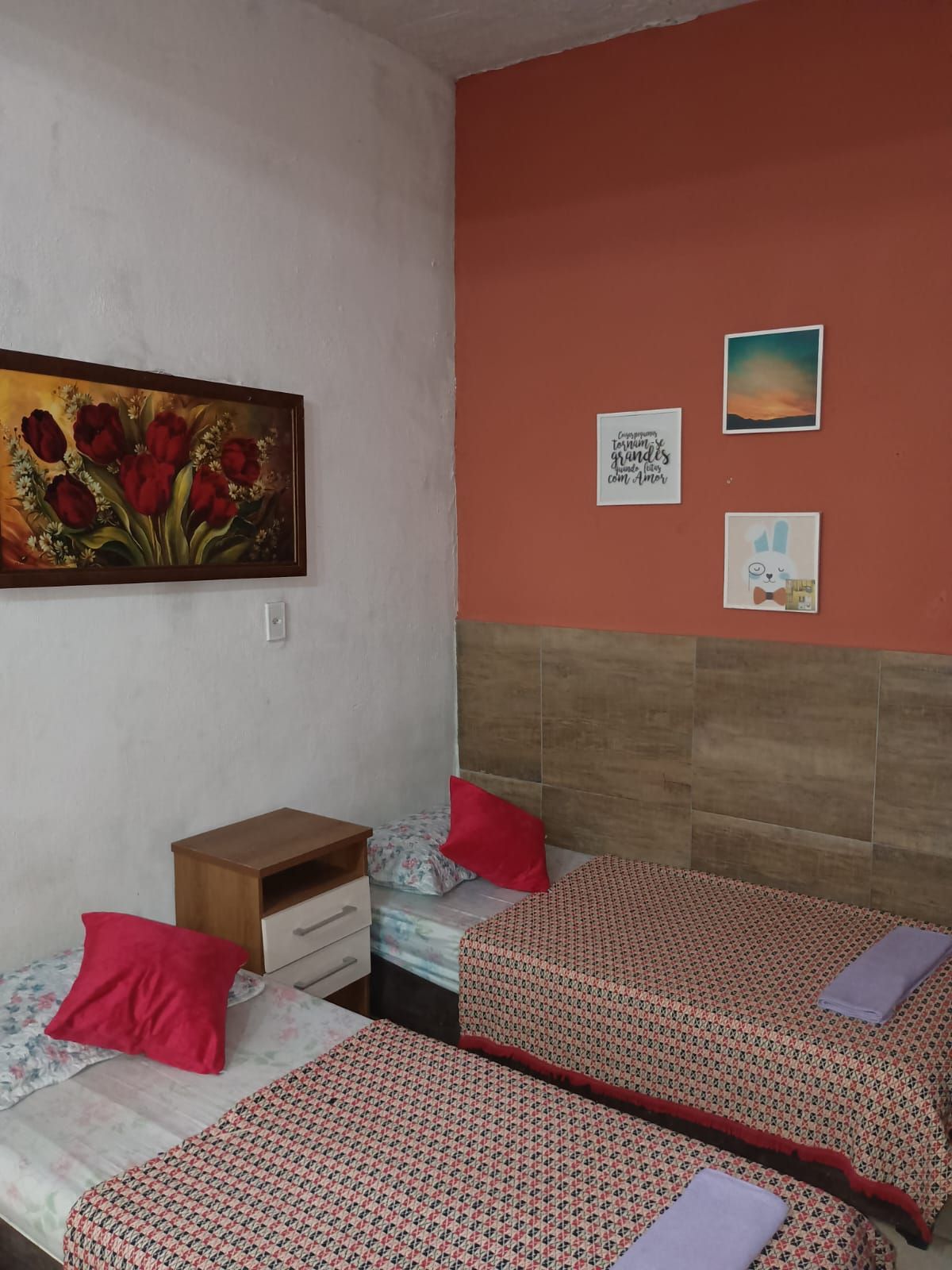 Un dormitorio con dos camas individuales, una mesita de noche, un cabecero de madera y un cuadro de flores rojas en la pared.
