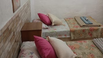 A small, simple room with two beds, each with floral bedding and pillows, a brick-patterned headboard, and two framed artworks on the wall.