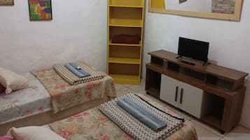 A room with two beds, a television on a wooden stand, a yellow shelf unit, and a mirror on the wall.