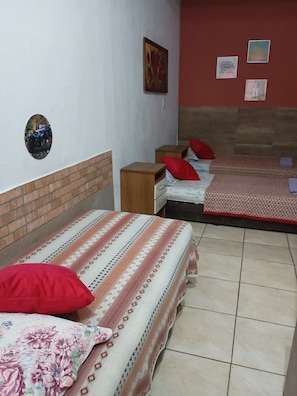 Una habitación con dos camas, cada una con cubrecama estampado y almohadas rojas, una mesita de noche de madera y una pared con un cuadro enmarcado y un espejo pequeño.