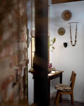A room with a brick wall, a wooden chair, a table with a vase, and wall decorations including a circular plate and a hanging necklace. - Secret Garden Stay – Minusha (Forestville)