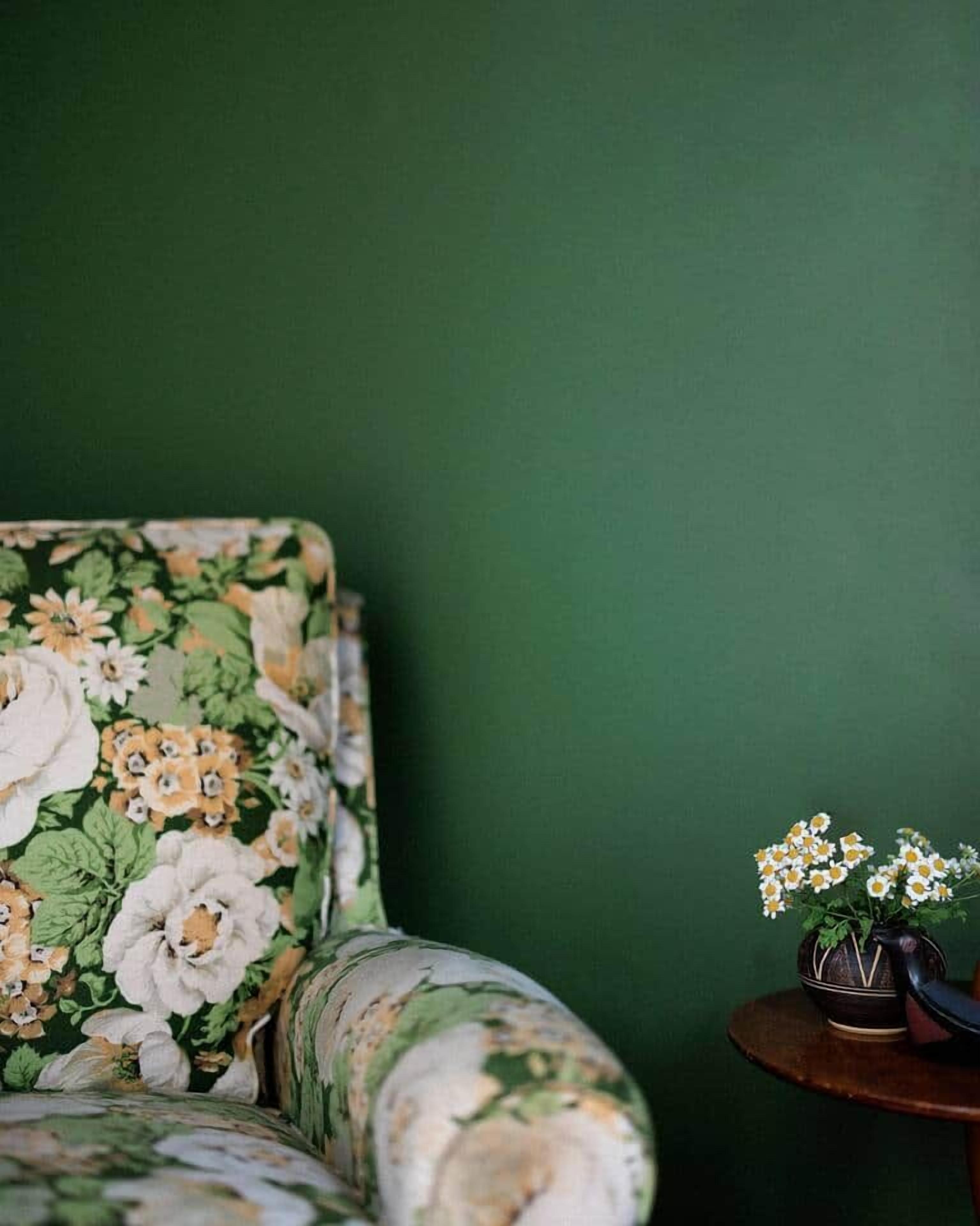 A room with a floral-patterned sofa against a green wall, a small round table with a vase of flowers.