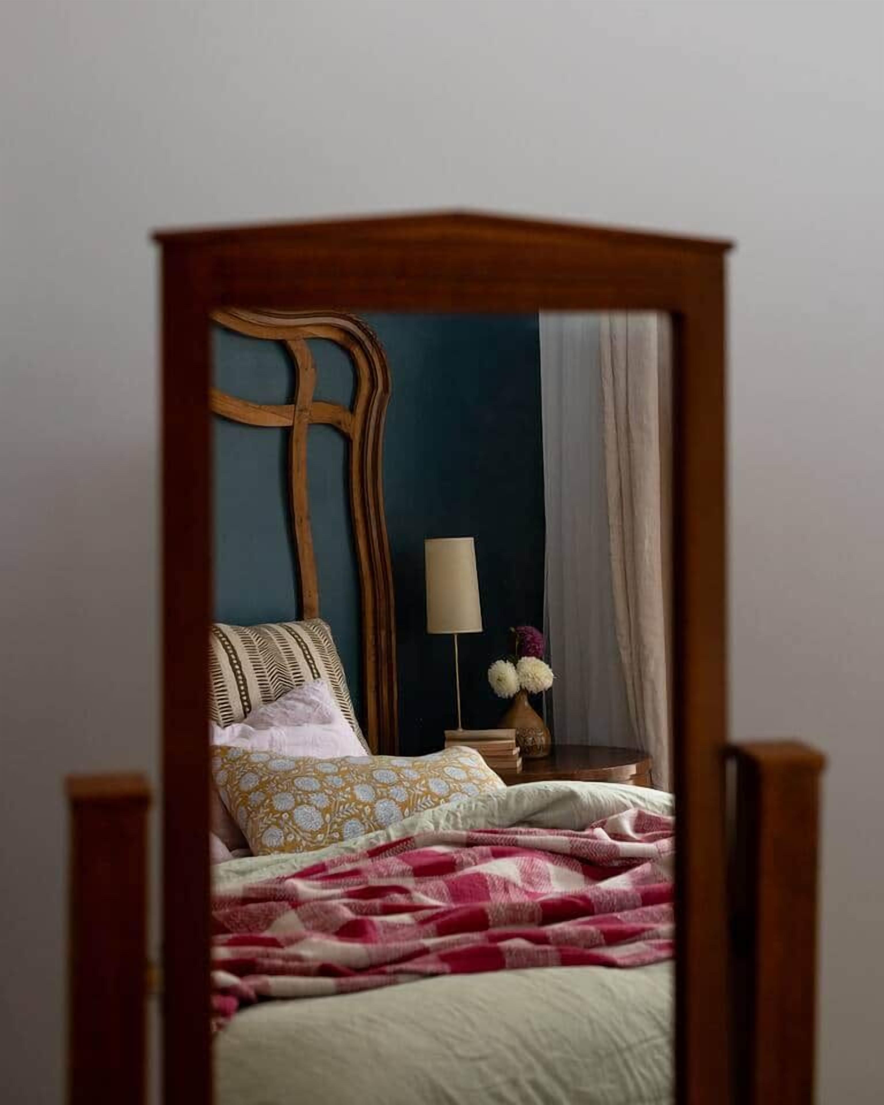 A bedroom with a wooden headboard, a bedside table with a lamp, and a bed with patterned bedding.