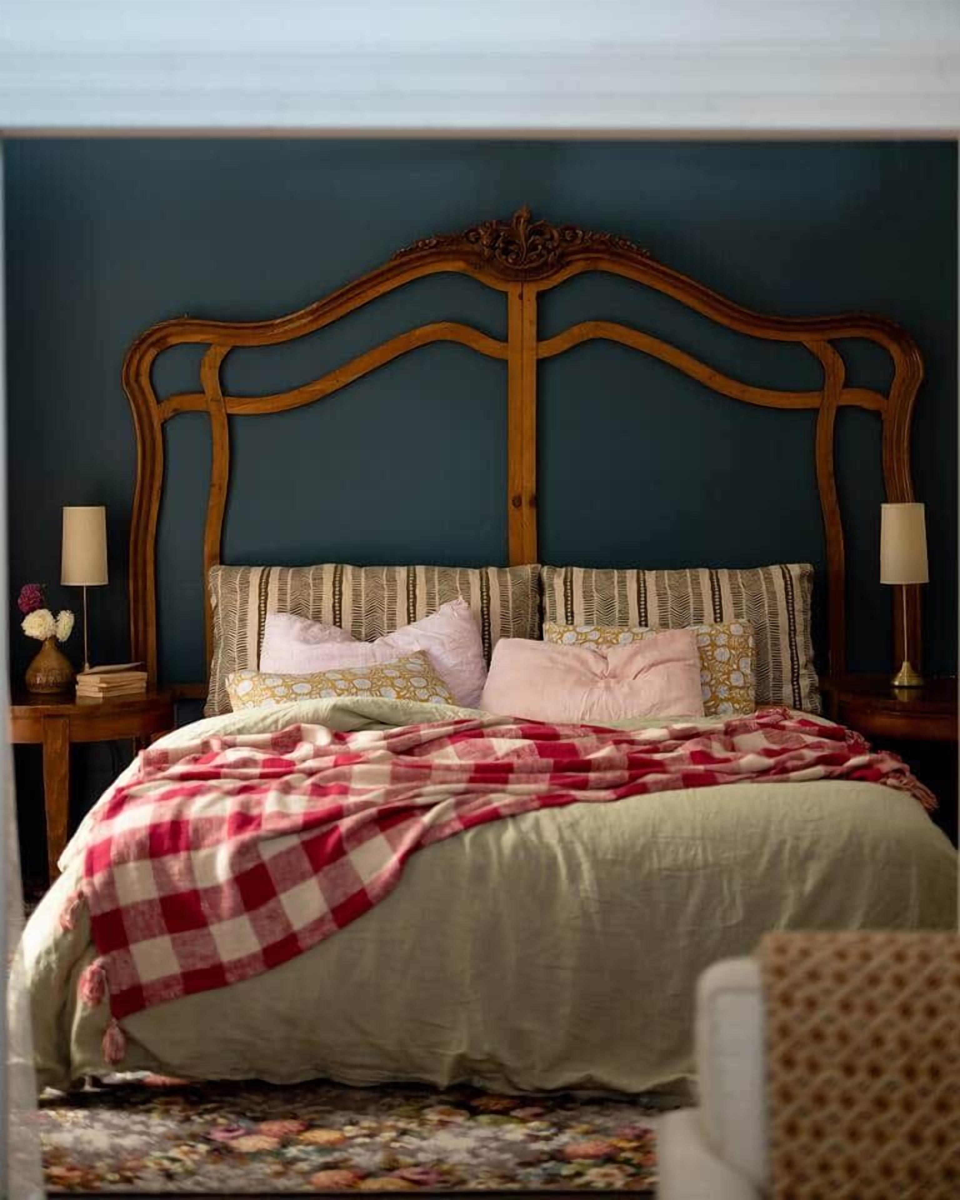 A bedroom with a wooden headboard, a bed with a checkered blanket, multiple pillows, and bedside lamps.