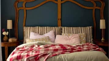 A bedroom with a wooden headboard, a bed with a checkered blanket, multiple pillows, and bedside lamps.