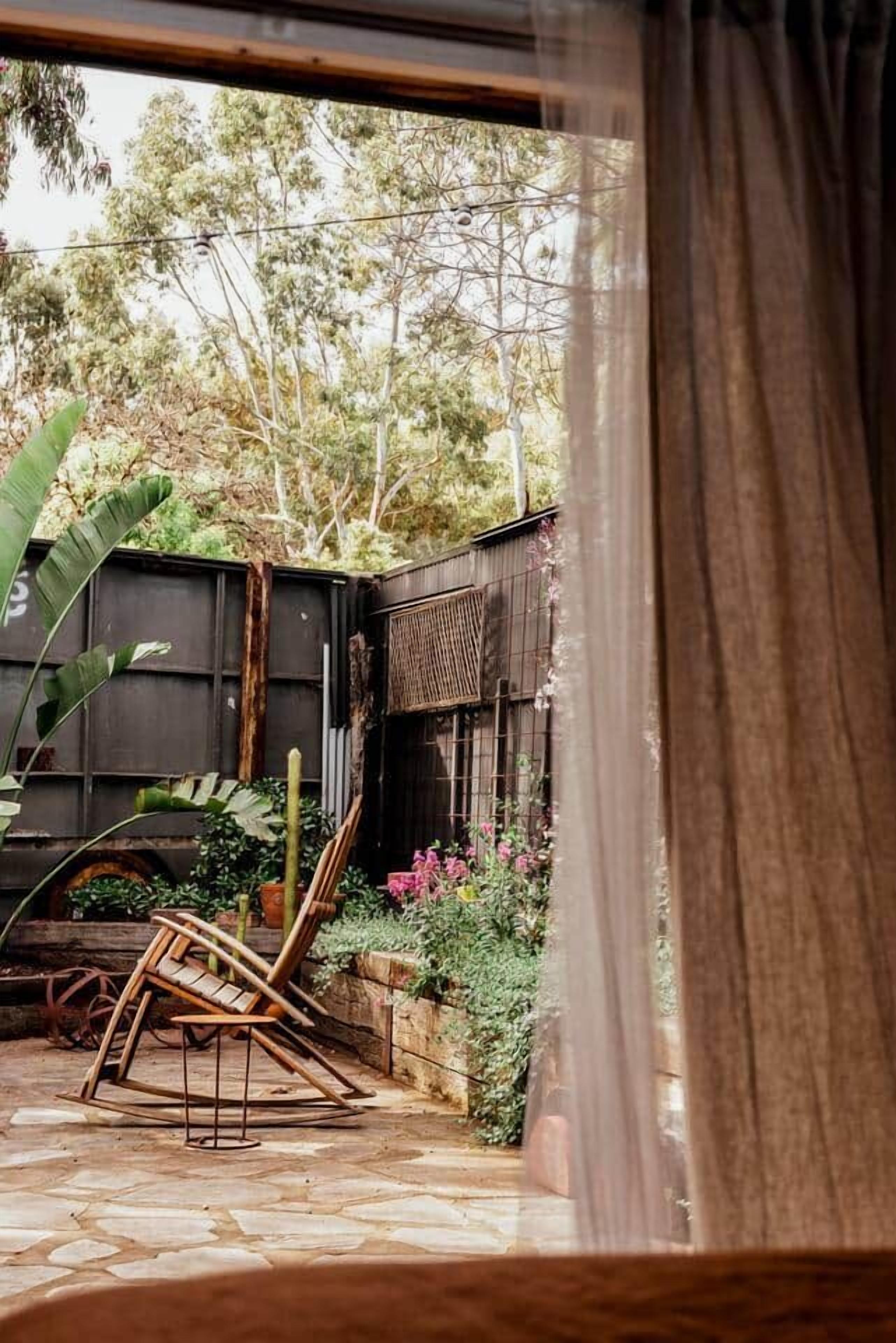 A rustic outdoor area with a stone floor, a wooden swing, and a metal chair.