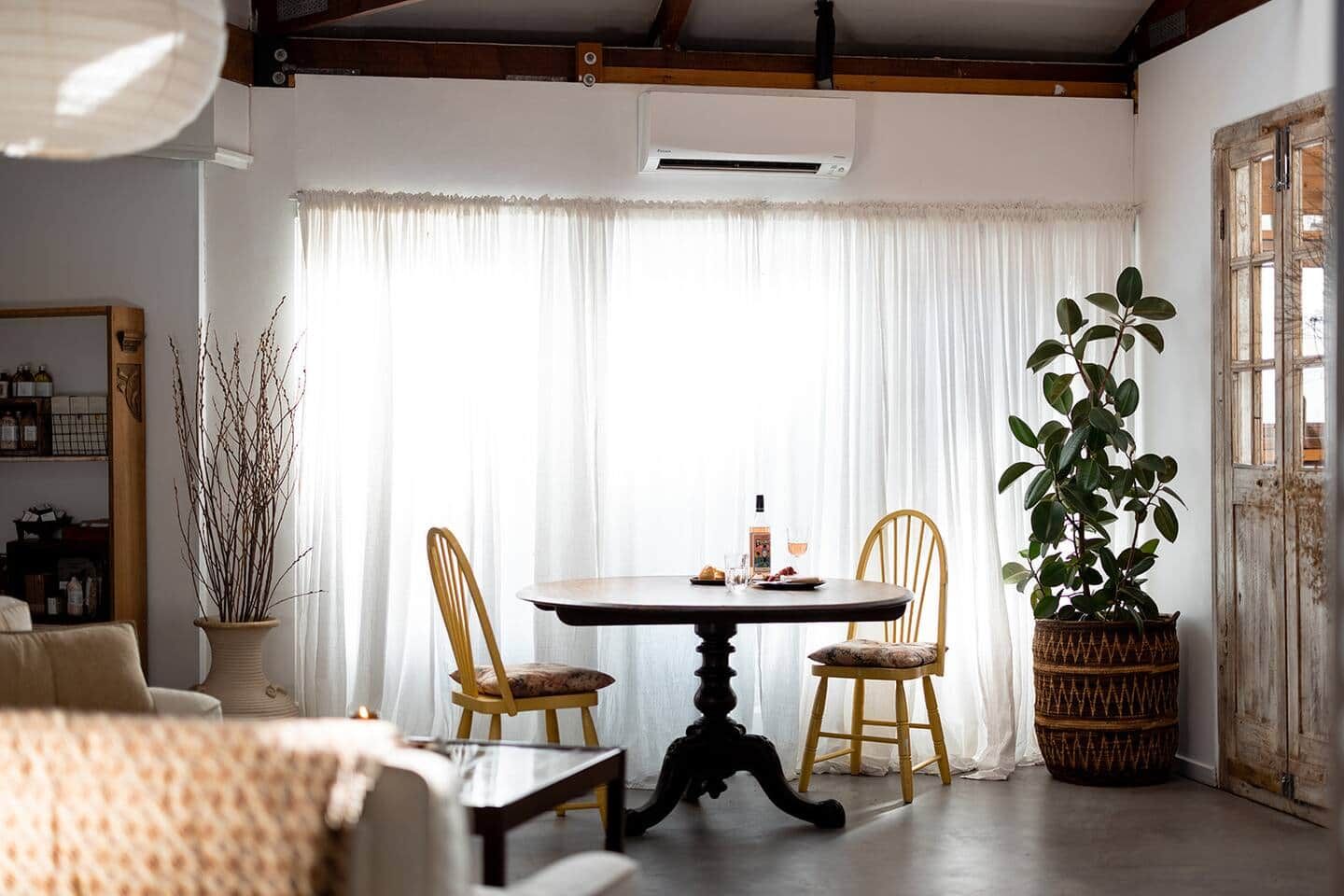 A dining area with a table and chairs, a potted plant, and a window with curtains.