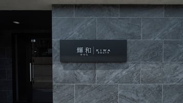 A black sign with white text on a grey stone wall, indicating the name 'KIWA SOUTH' and the word 'SAWUS'.