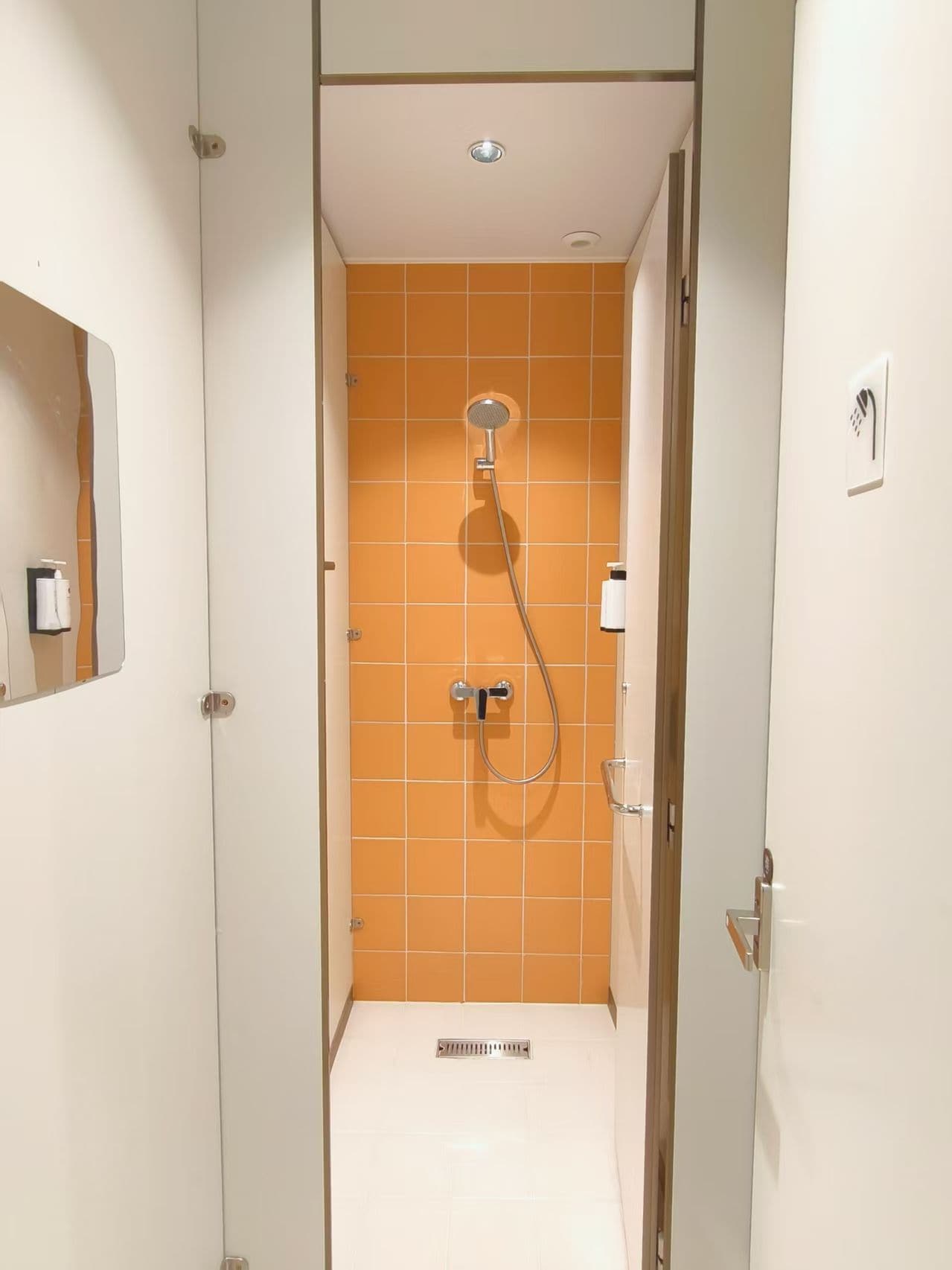 Un baño estrecho con ducha, paredes blancas y azulejos naranjas.