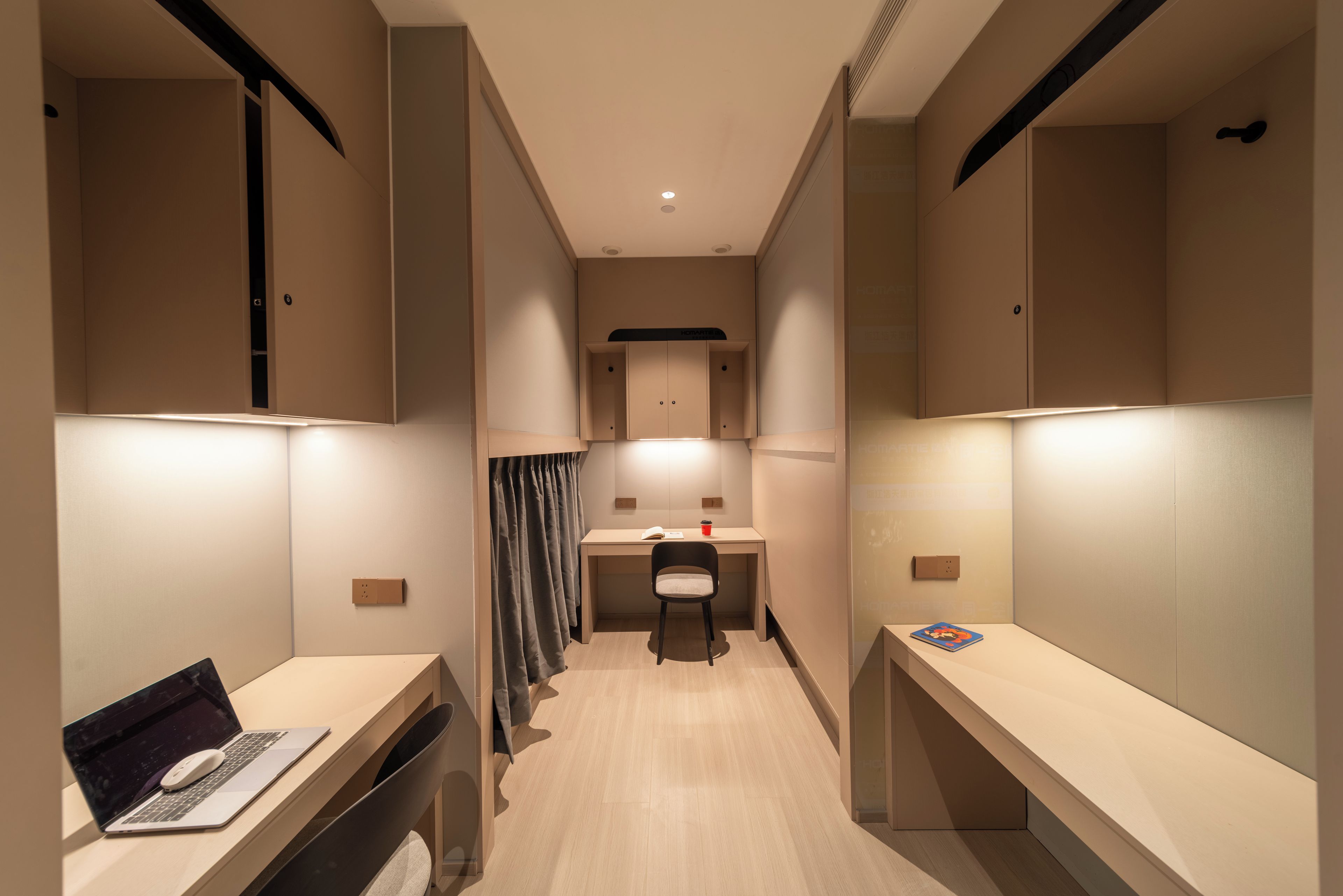 A modern hotel room with a desk, laptop, and a small table with a book.