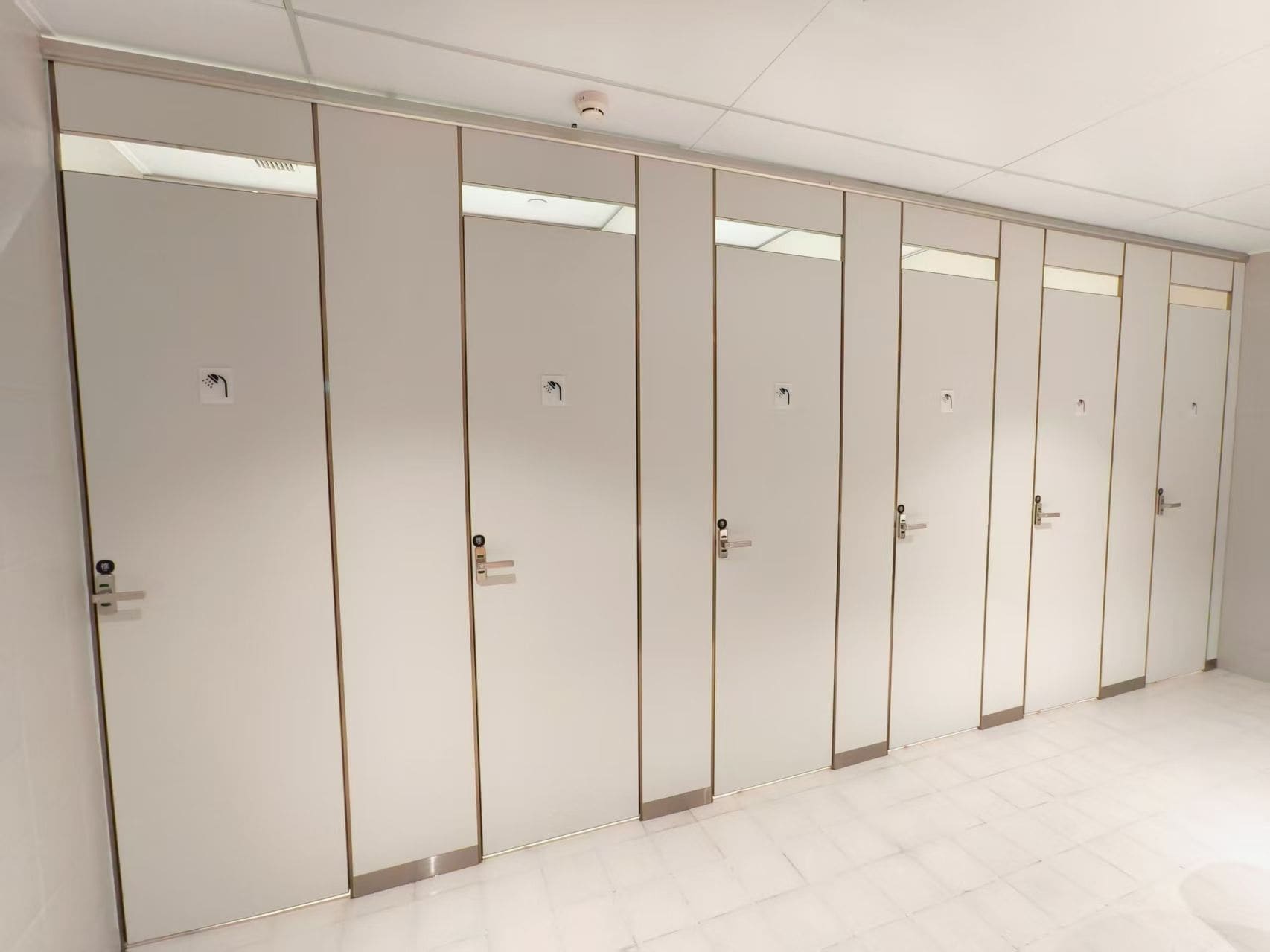 A row of white, wall-mounted cabinets with handles, likely for storage, in a clean, tiled room.