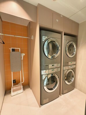 A laundry room with two wall-mounted washing machines, a drying rack, and a wall-mounted heater.