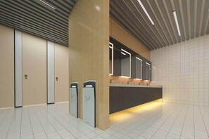 Un baño moderno con un mostrador largo, dos secamanos y un espejo sobre el lavabo.