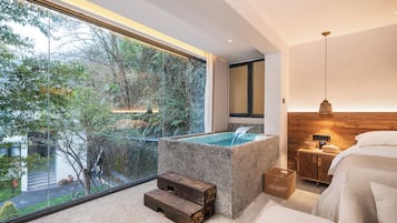 A modern bathroom with a freestanding bathtub, a wooden bench, and a view of a lush garden through a large window.