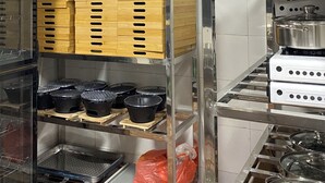 Cozinha com eletrodomésticos de aço inoxidável, prateleiras de madeira e recipientes de plástico.