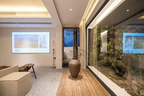 Un vestíbulo moderno con una gran pantalla de proyección, un jarrón grande con ramas y una pared de vidrio con plantas.
