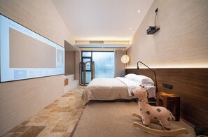 A modern hotel room with a large bed, a projector screen, and a wooden rocking horse.