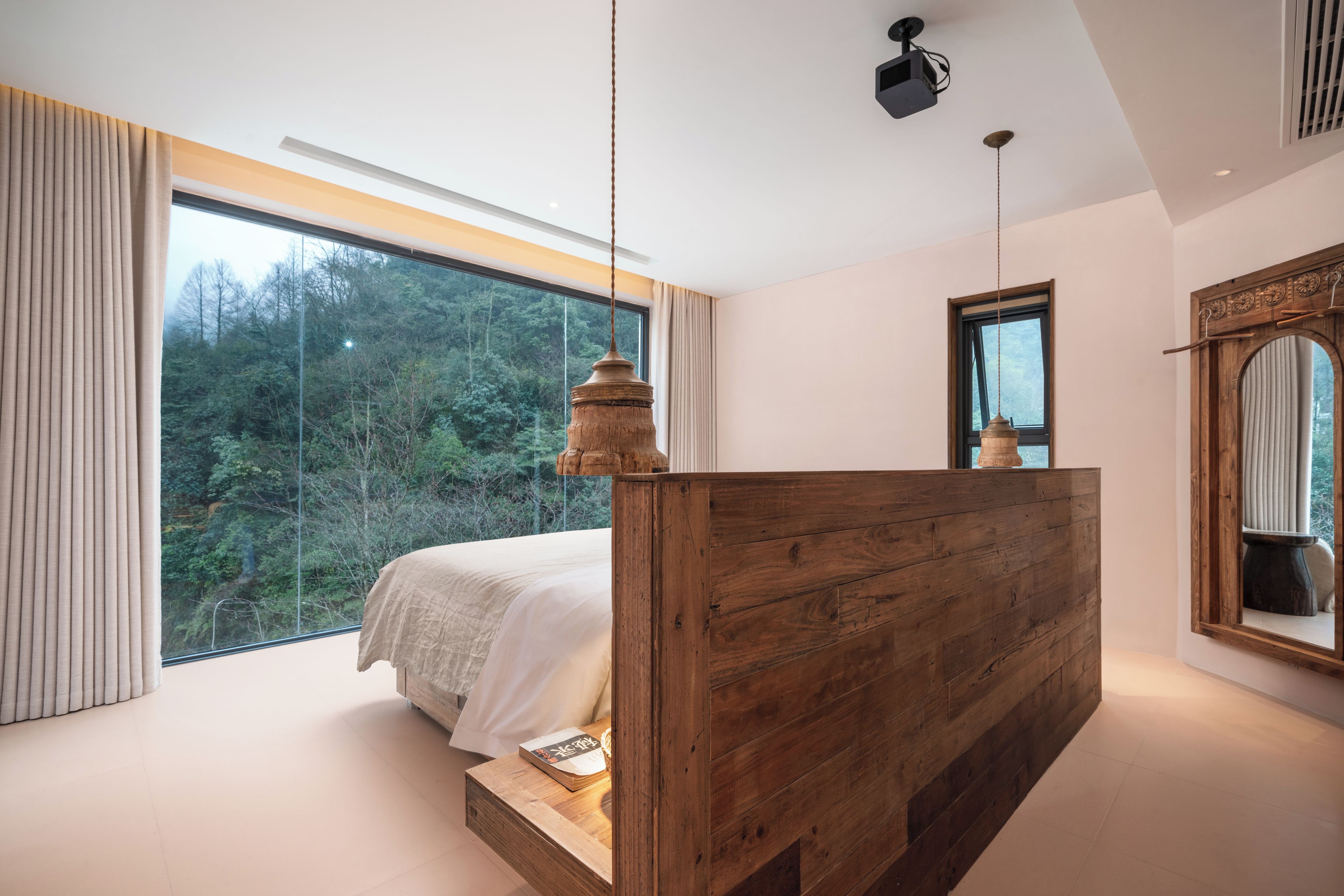 A bedroom with a large window, a wooden bed frame, and a view of a forest.
