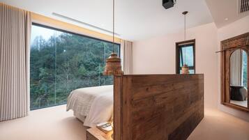 Un dormitorio con un ventanal grande, un cabecero de madera y vistas a un bosque.