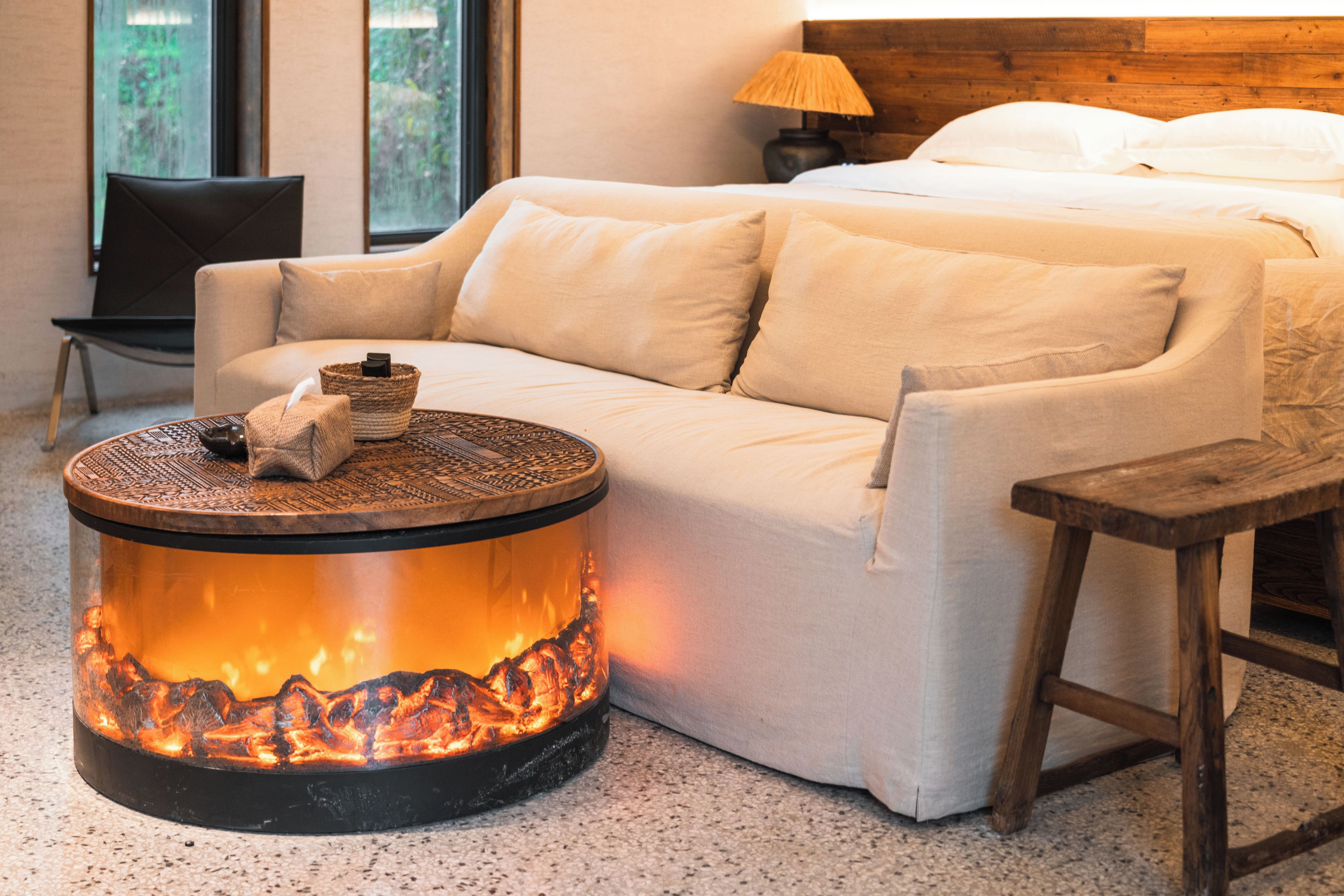 Una habitación acogedora con cama, sofá, una pequeña mesa redonda con fuego y una silla.