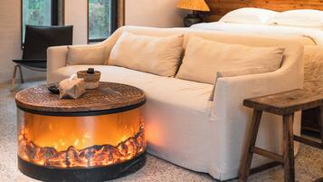 Una habitación acogedora con cama, sofá, una pequeña mesa redonda con fuego y una silla.