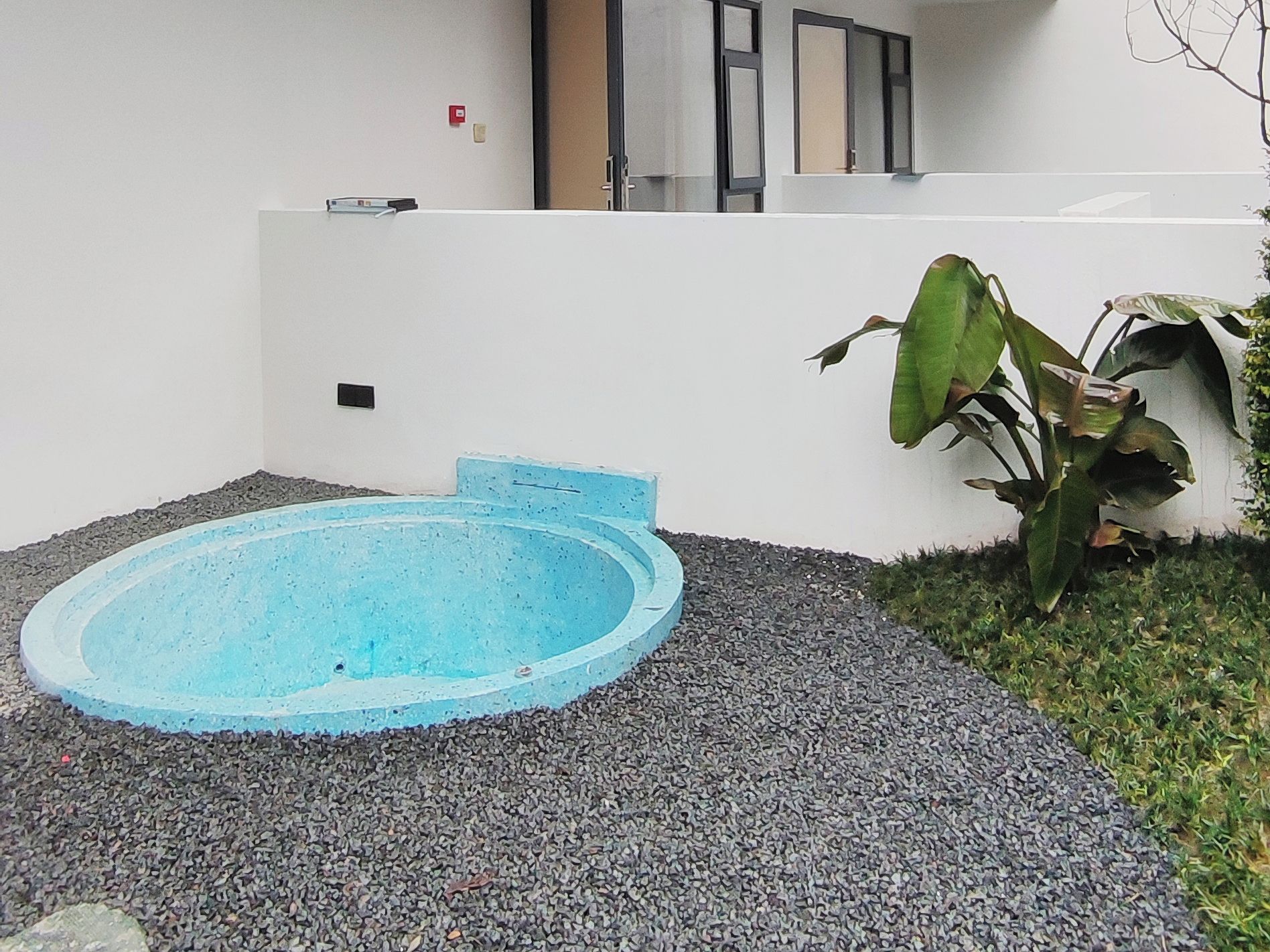A small, round, blue pool with a shallow edge, surrounded by gravel and a white wall.