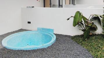 A small, round, blue pool with a shallow edge, surrounded by gravel and a white wall.