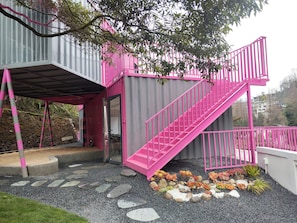 A pink and gray building with a staircase and a garden area with rocks and plants.