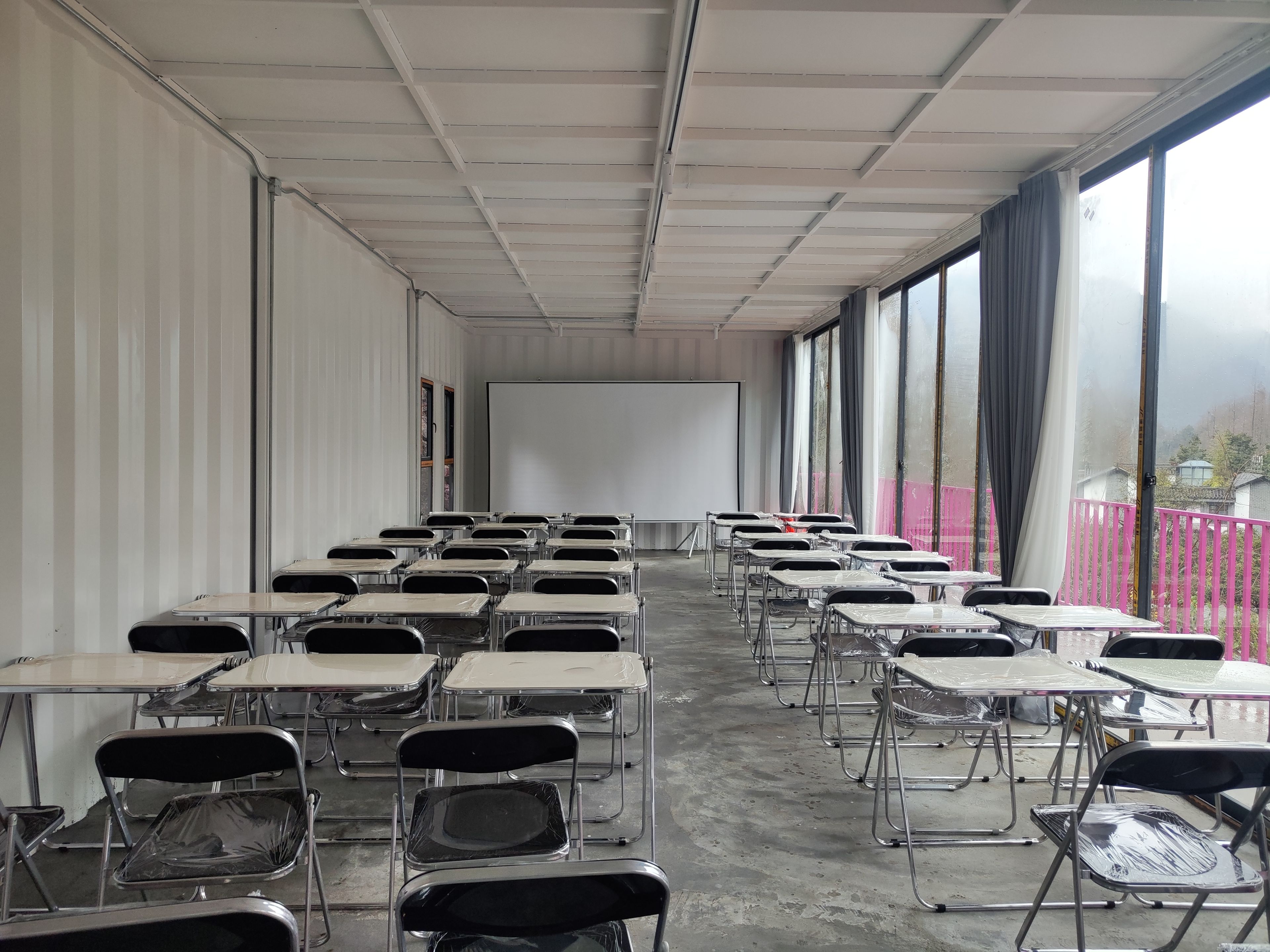 A classroom with rows of desks and chairs, a whiteboard, and large windows.