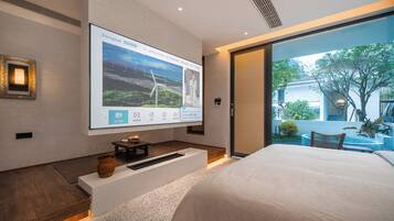 Un dormitorio moderno con una cama grande, un televisor de pantalla plana con un paisaje escénico y vistas a un jardín a través de una puerta corredera.