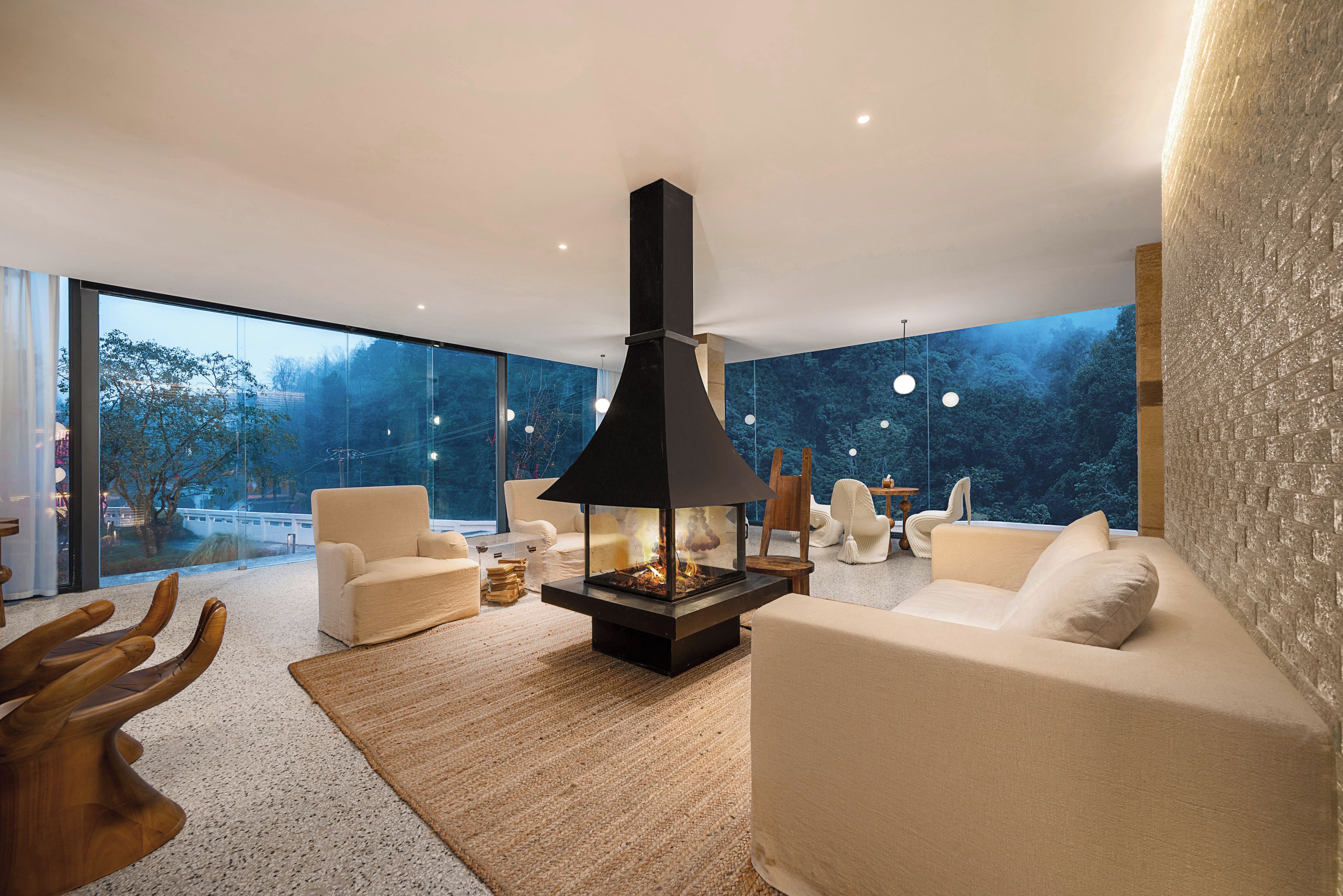 Una sala de estar moderna con chimenea, asientos cómodos y ventanas amplias que ofrecen vistas a árboles.