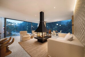 Una sala de estar moderna con chimenea, asientos cómodos y ventanas amplias que ofrecen vistas a árboles.